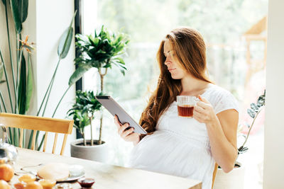 Young modern pregnant business woman working on a tablet at breakfast. 