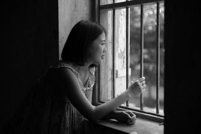 Young woman looking through window at home