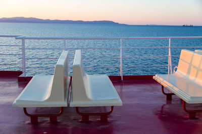 Chairs on table by swimming pool against sky during sunset