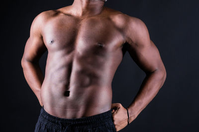 Midsection of shirtless man standing against black background