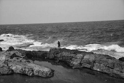 Man standing on rock by sea against clear sky