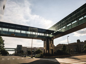 Low angle view of elevated walkway by buildings against sky