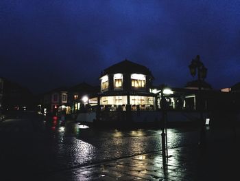 Illuminated buildings by street against sky at night