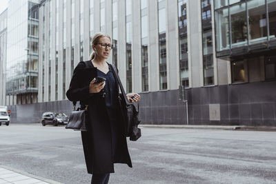 Contemplating businesswoman with smart phone walking in city
