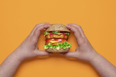 Close-up of hand holding ice cream against orange background