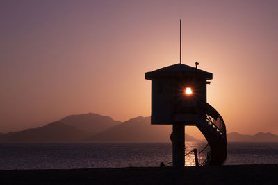 Silhouette house by sea against sky during sunset