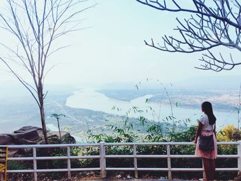 Rear view of woman standing by railing against sky