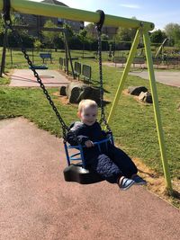 Portrait of boy swinging at playground during sunny day