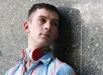 Man wearing headphones while leaning on wall