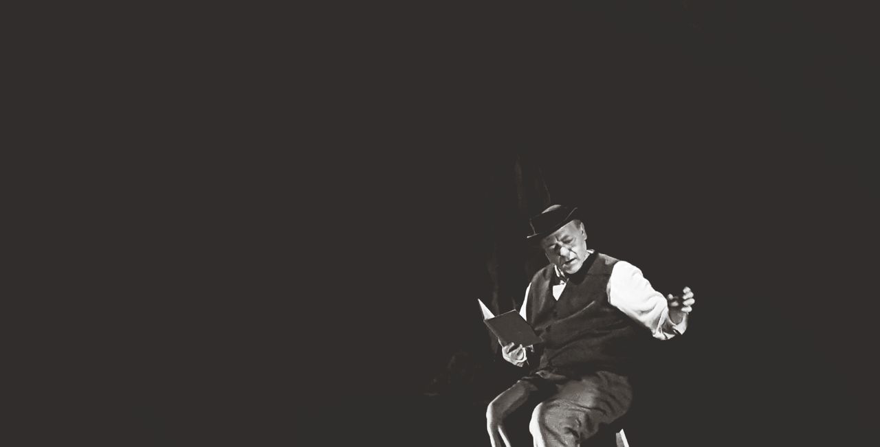 MAN SITTING AGAINST BLACK BACKGROUND