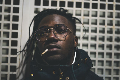 Young man looking away while smoking cigarette against metal grate