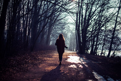 Rear view of woman walking on footpath amidst bare trees