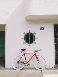 Bicycle parked against white wall of building
