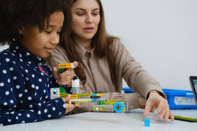 Multiethnic kids at stem lesson constructing robot in classroom with woman teacher children making