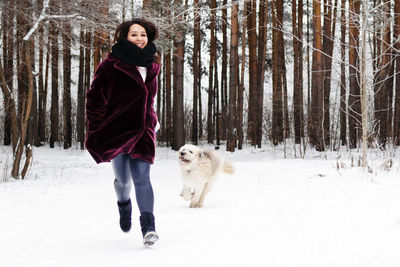 Beautiful woman is running with her south russian shepherd dog on a background of winter forest.