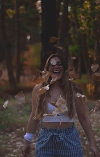 Cheerful woman with mouth open throwing leaves in forest