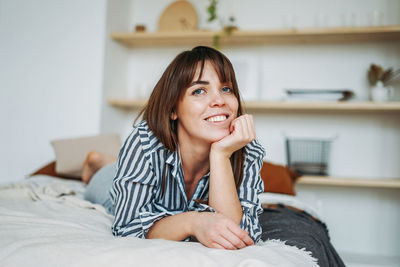 Portrait of smiling young woman lying on bed at home