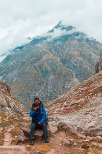 Man sitting on mountain against sky