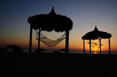 Silhouette built structure on beach against sky during sunset