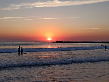 Silhouette people on beach against sky during sunset