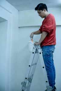 A young man taking white paint from a pot, on stairs