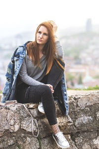 Full length of thoughtful woman sitting on retaining wall