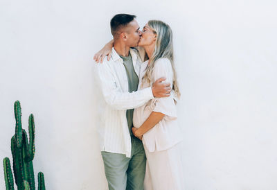 Happy man kissing his pregnant wife outside against a white wall.