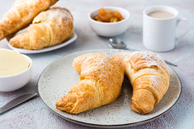 A pair of fresh crispy croissants on a plate, a cup of coffee and bowls of jam and butter 