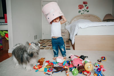 Funny baby toddler girl with toy bin on head. kid child playing with toys at home. 