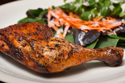 Close-up of grilled chicken leg with mixed salad served in plate