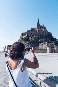 Woman photographing with mobile phone against sky