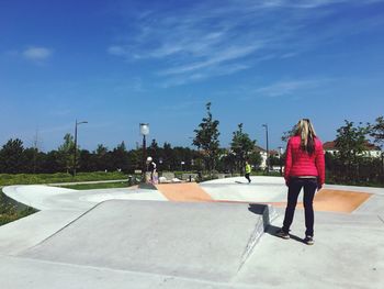 Rear view of woman standing at park against blue sky during sunny day