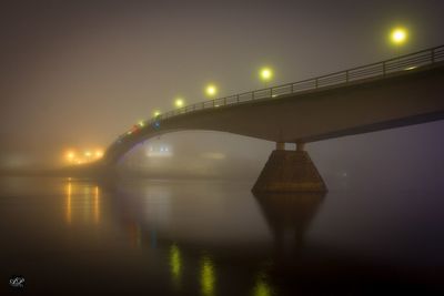 Illuminated bridge over river against sky at night