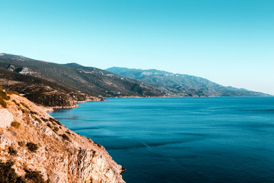 Scenic view of sea and mountains against clear blue sky