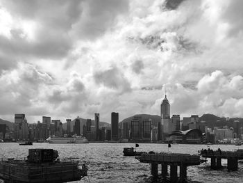 Boats in river with cityscape in background against cloudy sky