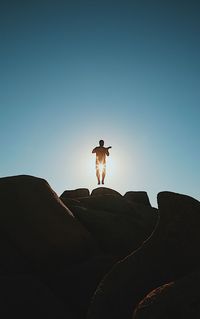 Silhouette mid adult man playing guitar while standing on rock formation against blue sky