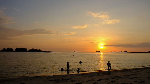 Silhouette people on beach against sky during sunset