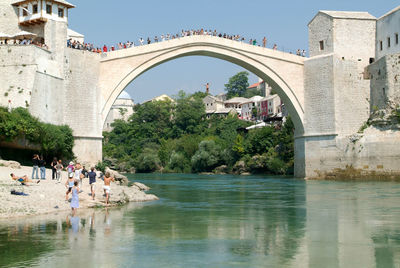 People on bridge over river against buildings