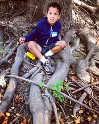 Portrait of happy boy playing on tree trunk