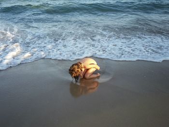 High angle view of shirtless boy kneeling on shore