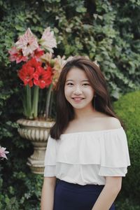 Portrait of smiling young woman standing against plants at park