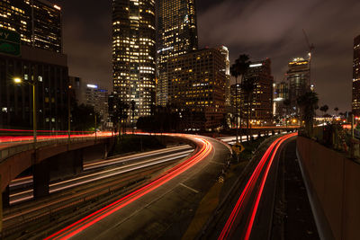 Light trails on bridge by illuminated buildings at night