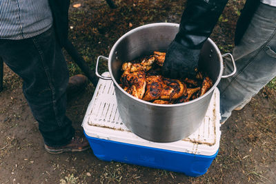 Low section of men with meat in container on field