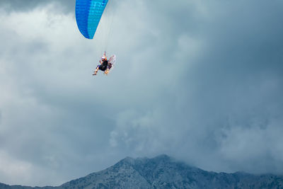 Person paragliding over mountain against sky