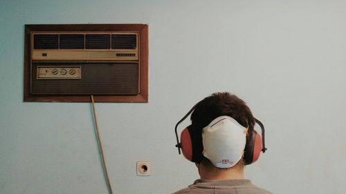 Rear view of man wearing ear muff against wall at home