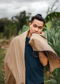 Portrait of young man with scarf standing against plants