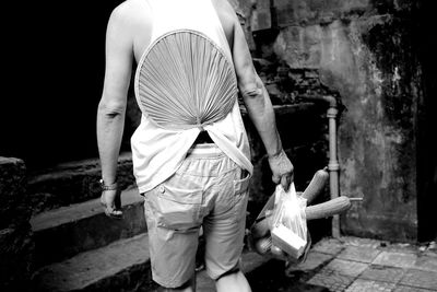 Rear view of man with hand fan inserted in pants carrying grocery bag