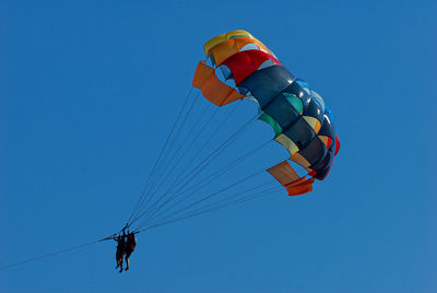 Low angle view of people paragliding against clear blue sky