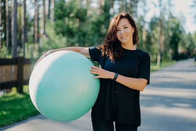 Portrait of smiling woman with fitness ball standing in park