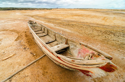 Damaged rowboat at beach against sky